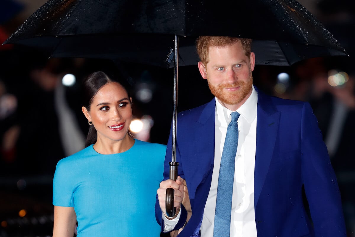 Meghan Markle and Prince Harry, whose reportedly diverging career paths could attribute to alleged 'tension' at home, per a commentator look on walking under an umbrella.