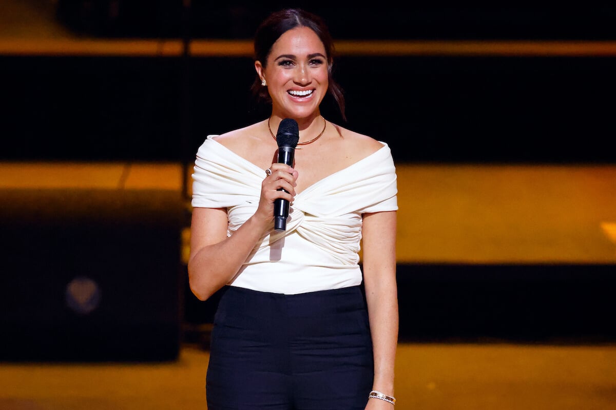 Meghan Markle, whose 2018 Royal Foundation Forum 'hitting the ground running' comment filled the palace with 'dread,' per a royal author, smiles holding a microphone