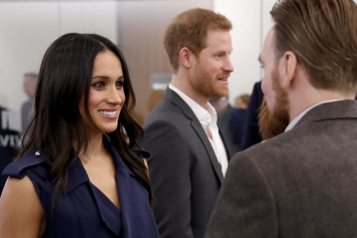 Meghan Markle, whose 'hitting the ground running' comment at the 2018 Royal Foundation Forum filled the palace with 'dread,' smiles standing next to Prince Harry