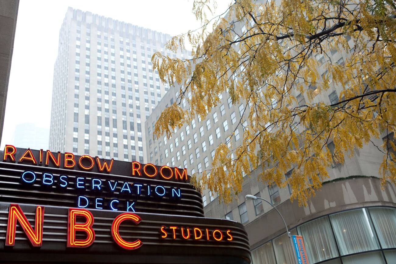 A photo of the NBC studios sign. There are buildings in the background and a yellow tree next to it. Sinéad O'Connor performed on 'SNL' here.