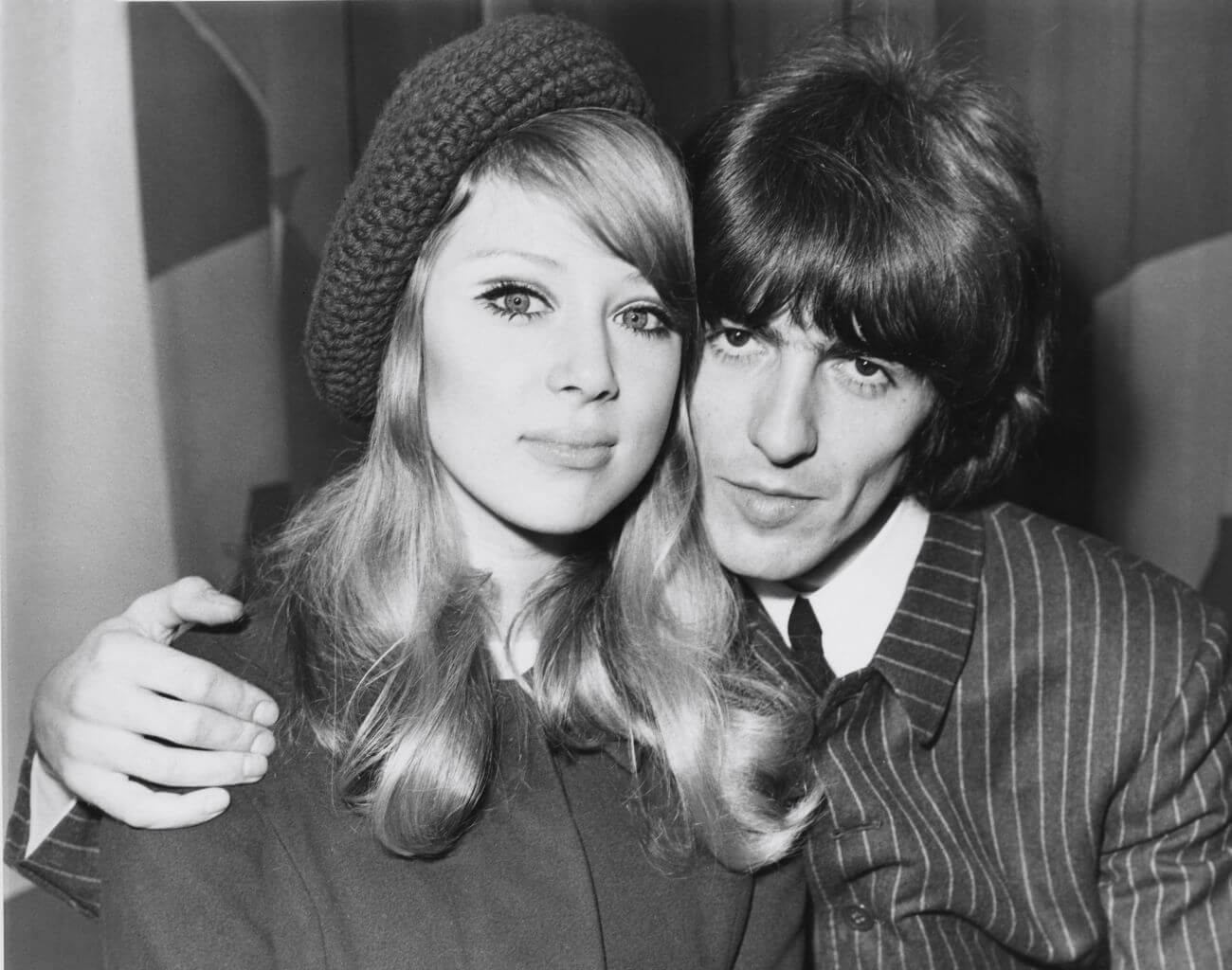 A black and white picture of George Harrison with his arm around Pattie Boyd's shoulders. She wears a knit hat.