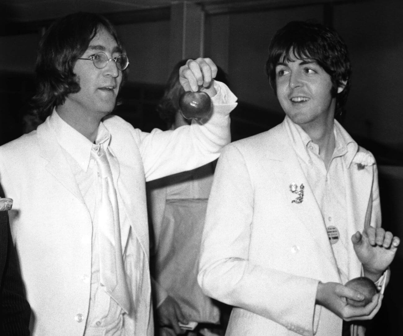 A black and white picture of John Lennon and Paul McCartney wearing white and holding apples.