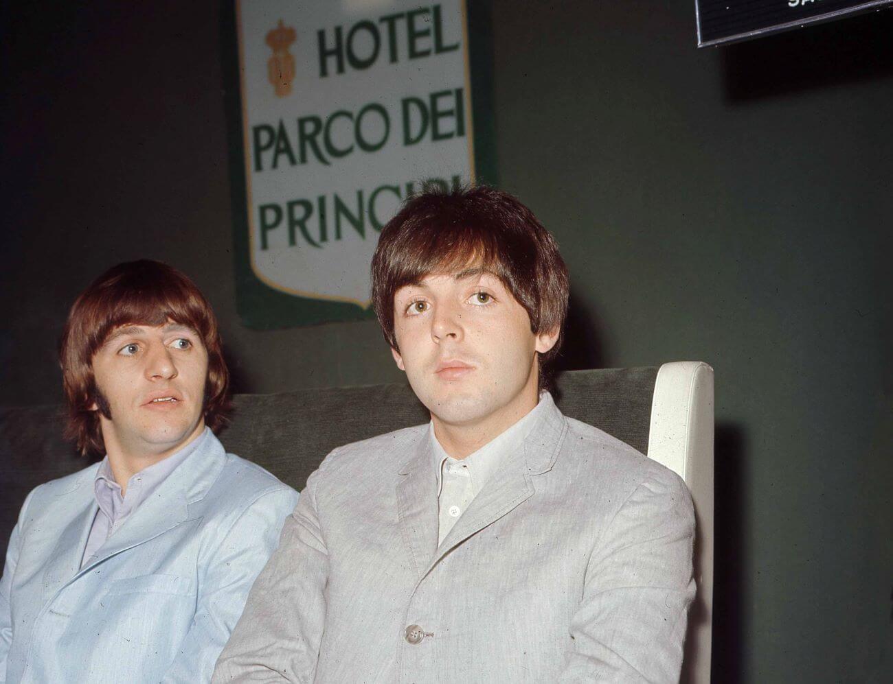 Ringo Starr and Paul McCartney sit at a table in front of a sign for the Hotel Parco dei Principi.