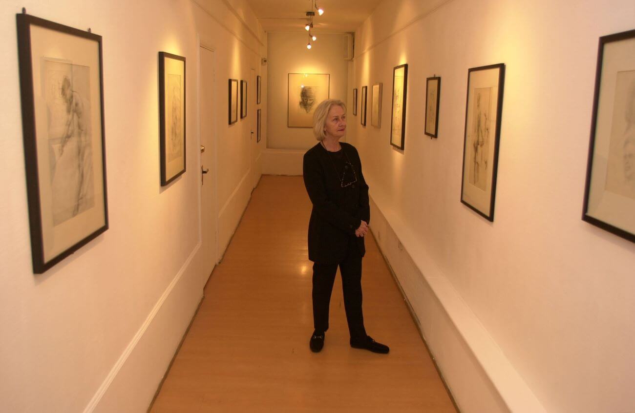 Stuart Sutcliffe's sister Pauline Sutcliffe stands in a gallery with sketches by her brother.