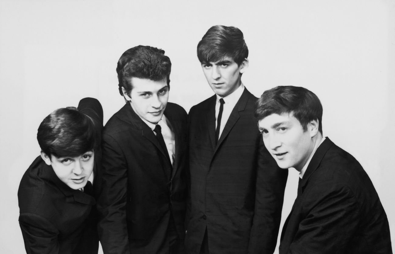 A black and white picture of Paul McCartney, Pete Best, George Harrison, and John Lennon wearing matching suits.