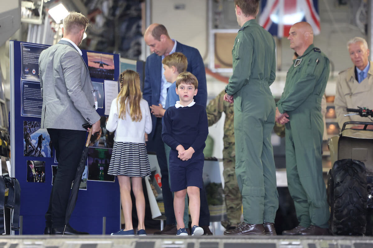 Prince Louis, whom a royal author says will have a more difficult time in the 'gilded cage' of royal life, stand swith Prince William, Princess Charlotte, and Prince George