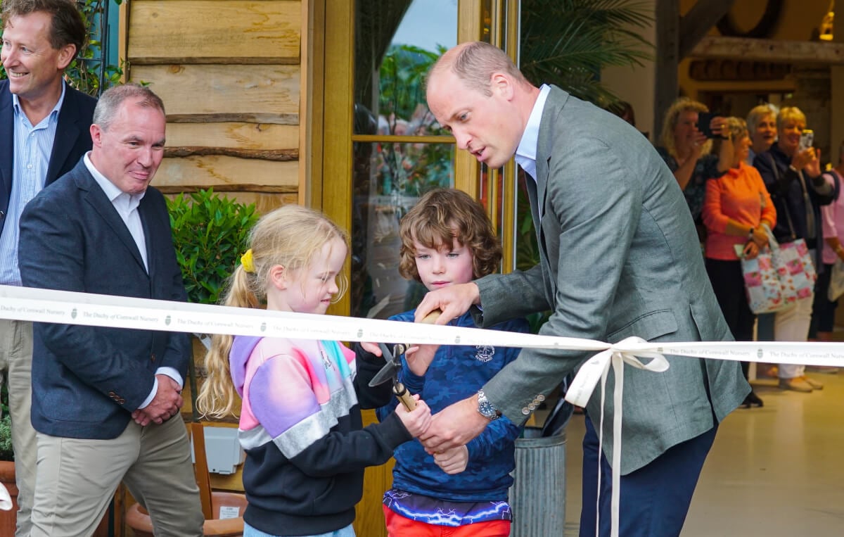 Prince William, Prince of Wales helps brother and sister James and Violet Scott to cut the ribbon as he visits The Duchy Of Cornwall Nursery to open The Orangery restaurant on July 10, 2023 in Lostwithiel, United Kingdom