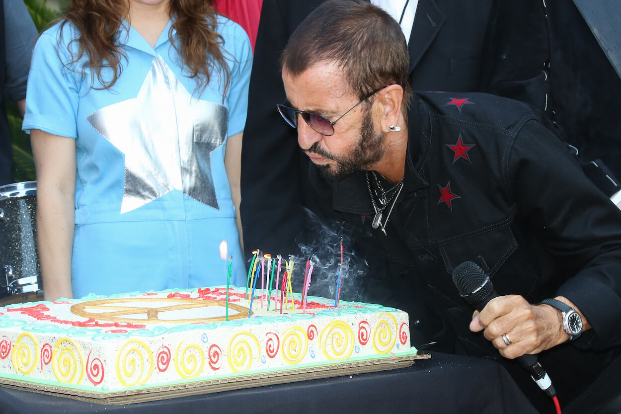 Ringo Starr bending over and blowing out candles on a cake during his 'Peace & Love' birthday celebration in 2017.