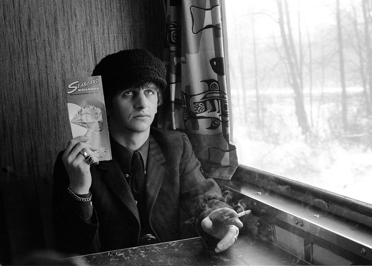 Beatles drummer Ringo Starr holding a cigarette and pamphlet while riding a train in 1964.