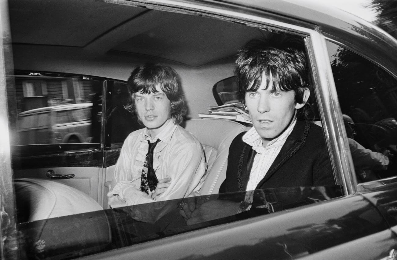 A black and white picture of Mick Jagger and Keith Richards sitting in the backseat of a car.