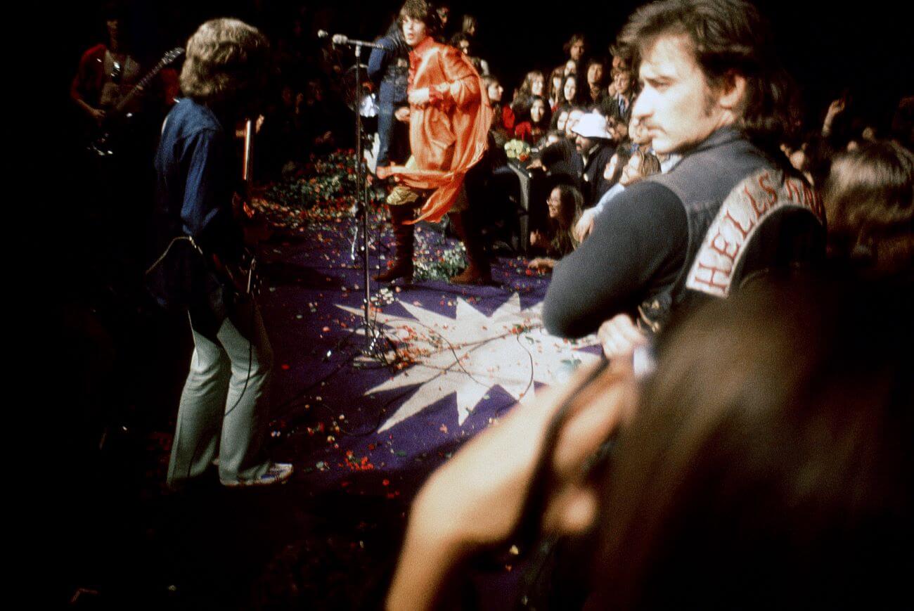 The Rolling Stones perform at the Altamont Free Concert while a member of the Hells Angels looks on.