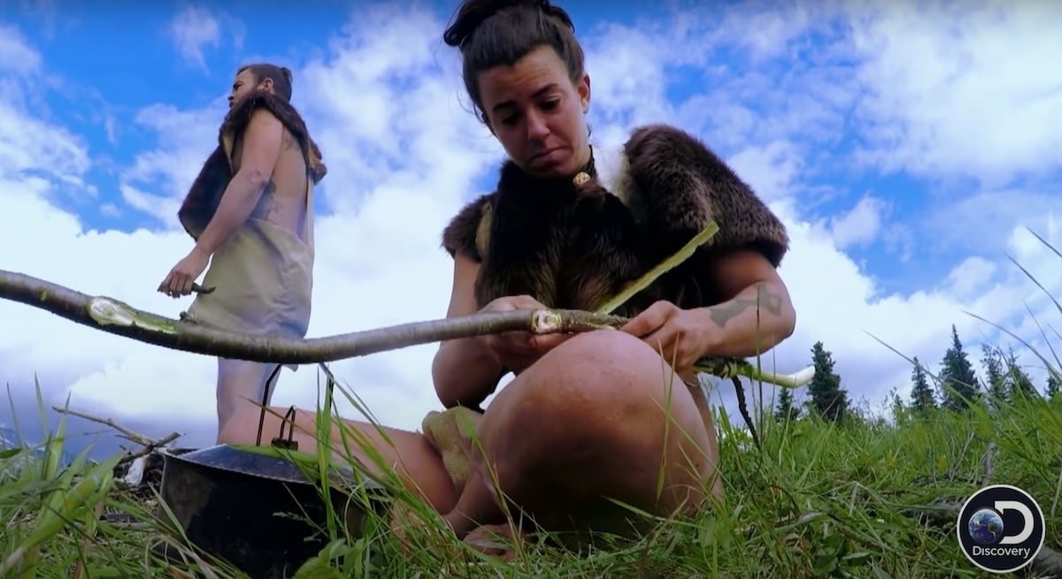 Laura sitting in front of a cooking pot with Steven standing in the background