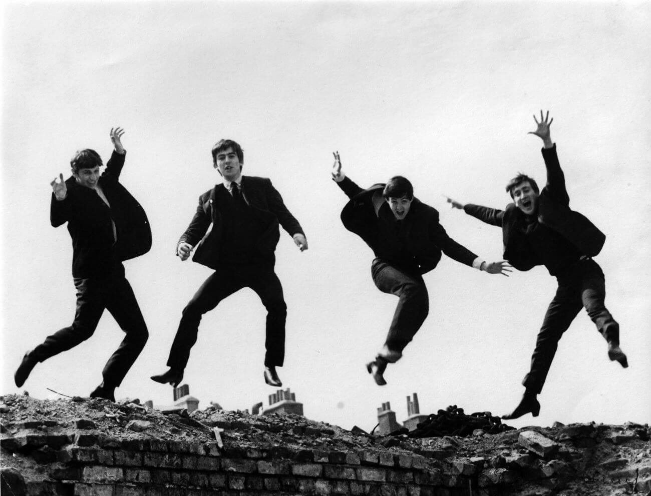 Ringo Starr, George Harrison, Paul McCartney, and John Lennon jump up in the air over a brick wall.