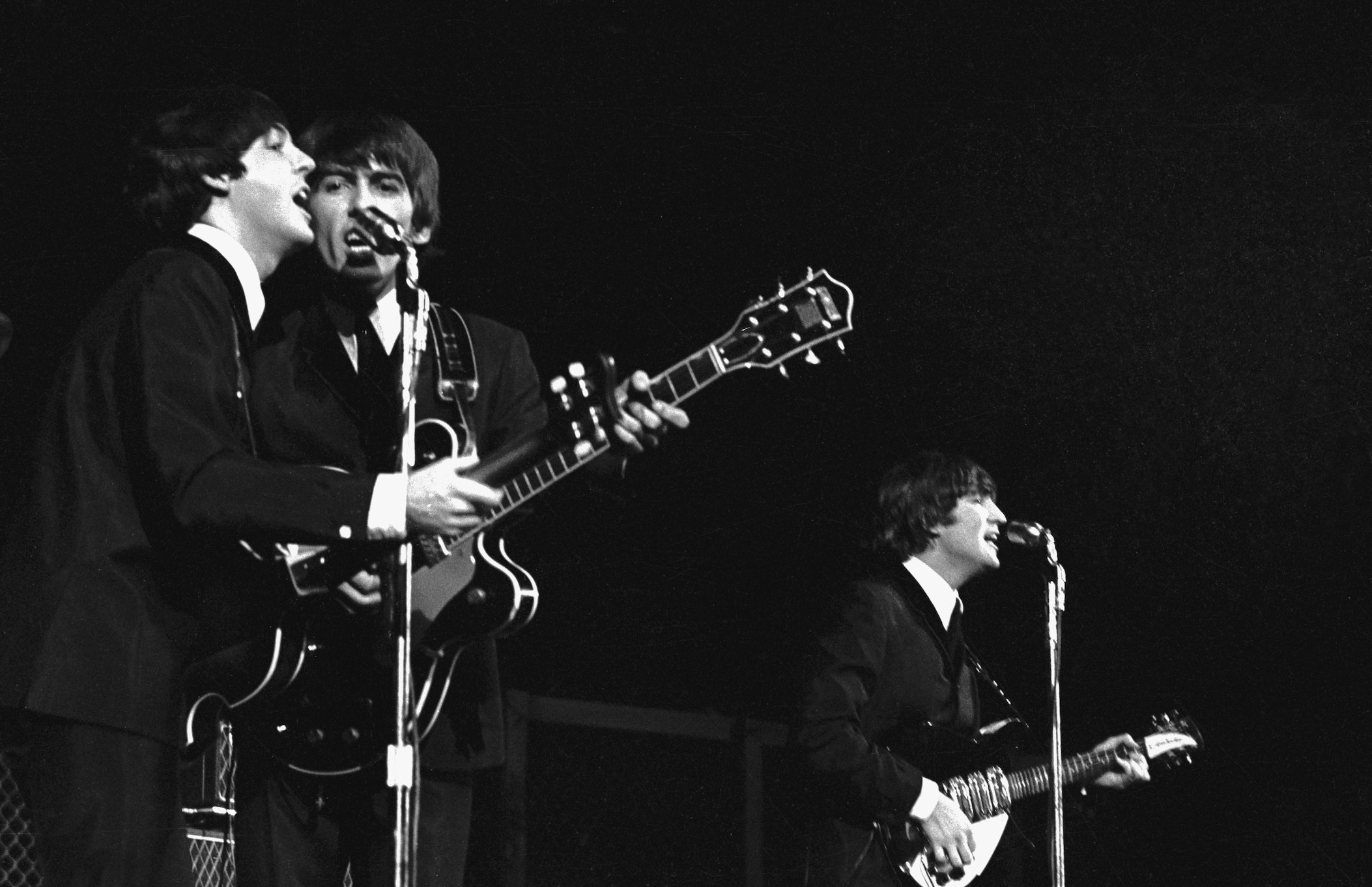 Paul McCartney, George Harrison, and John Lennon of The Beatles perform at a concert in America
