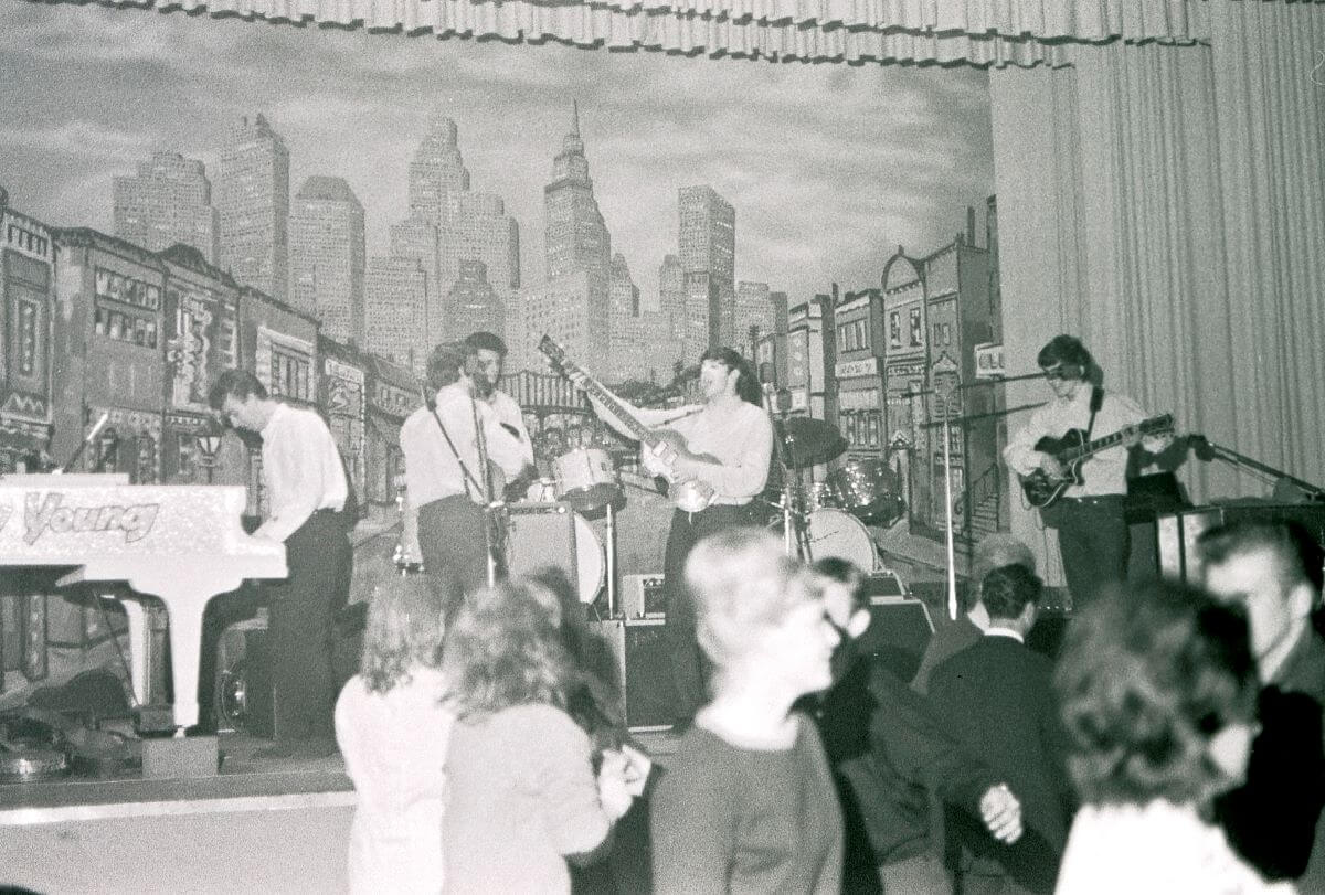A black and white picture of The Beatles performing onstage while an audience dances.