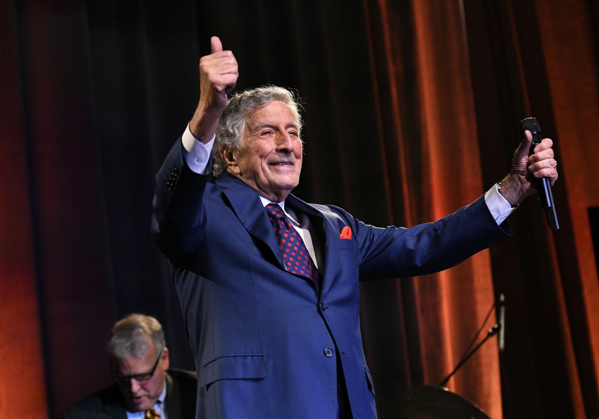 Tony Bennett in a suit holding two thumbs up and smiling