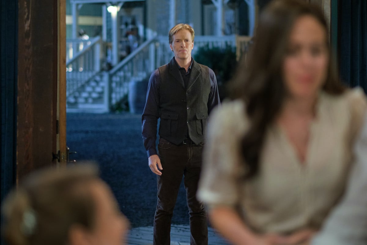 Bill standing in the background with out-of-focus Elizabeth in foreground in 'When Calls the Heart' Season 10