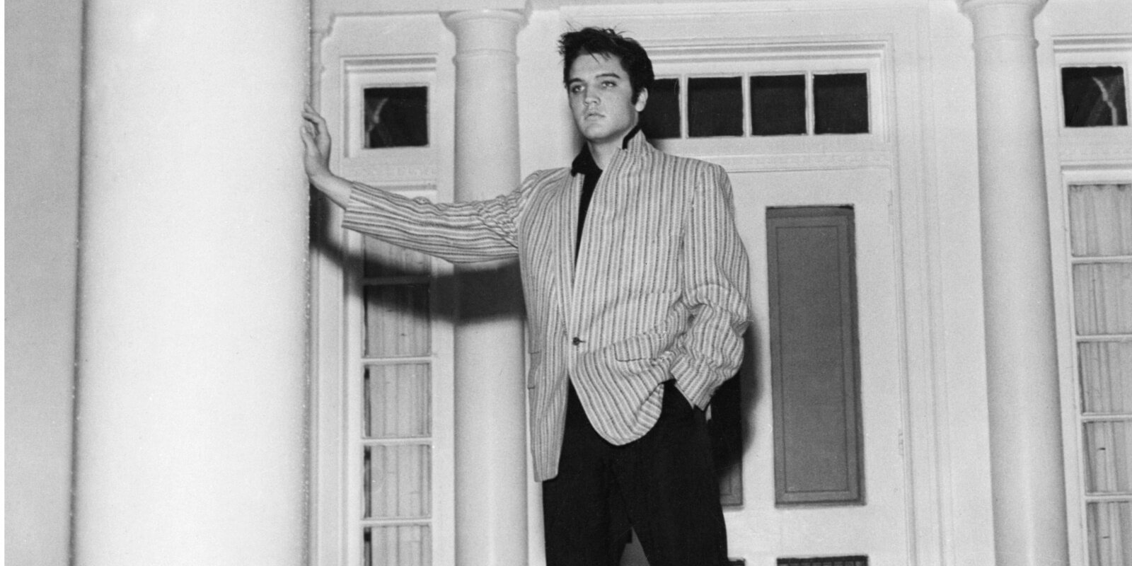 Elvis Presley leans on a column in front of his Graceland home in Memphis, TN.
