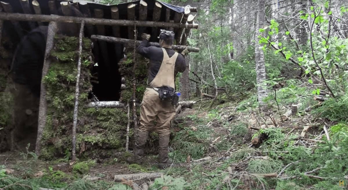 An 'Alone' cast member building a log cabin shelter