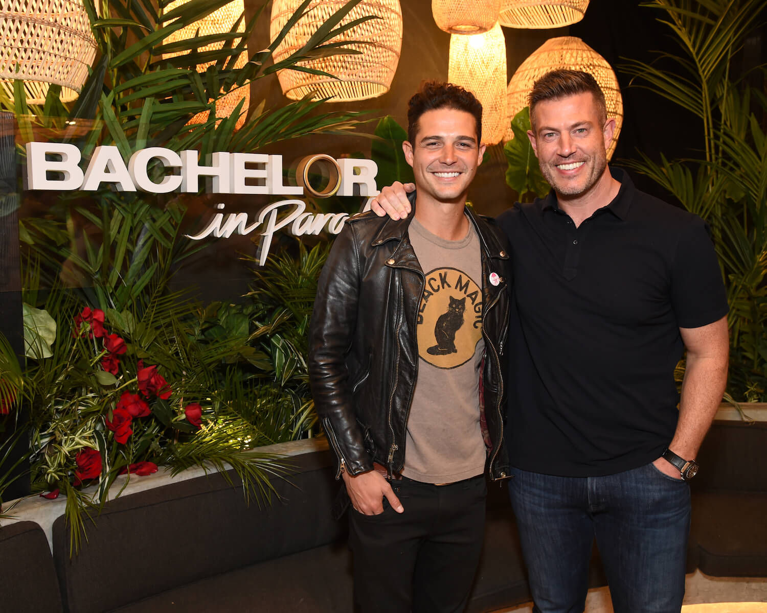 Jesse Palmer, the host of 'Bachelor in Paradise' Season 9, with his arm around Wells Adams in front of a 'Bachelor in Paradise' sign