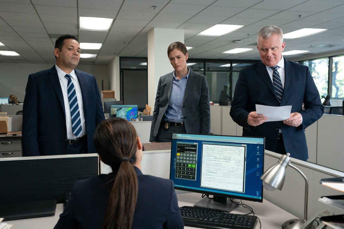 Two men and a woman in suits standing in front of a woman sitting at a desk in 'Bosch: Legacy' Season 2