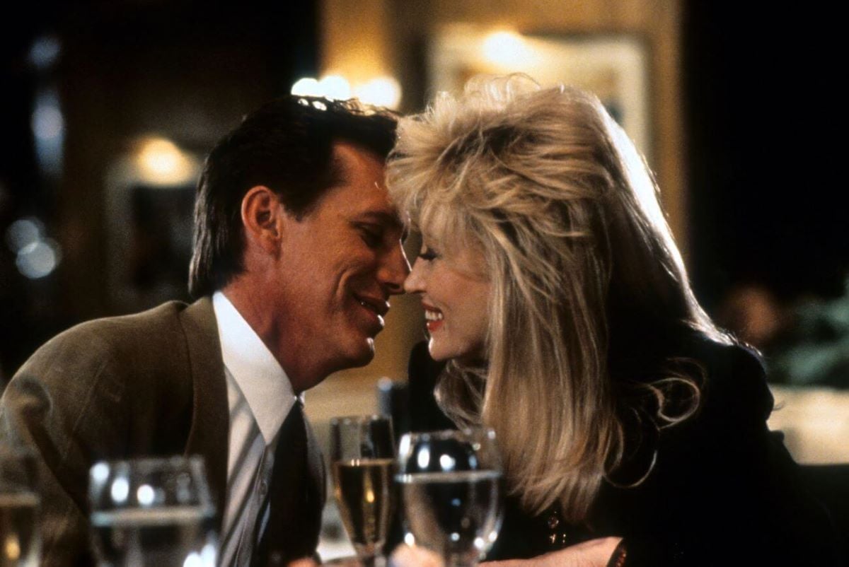 James Woods and Dolly Parton sit at a table and lean in to kiss each other in the film 'Straight Talk.'