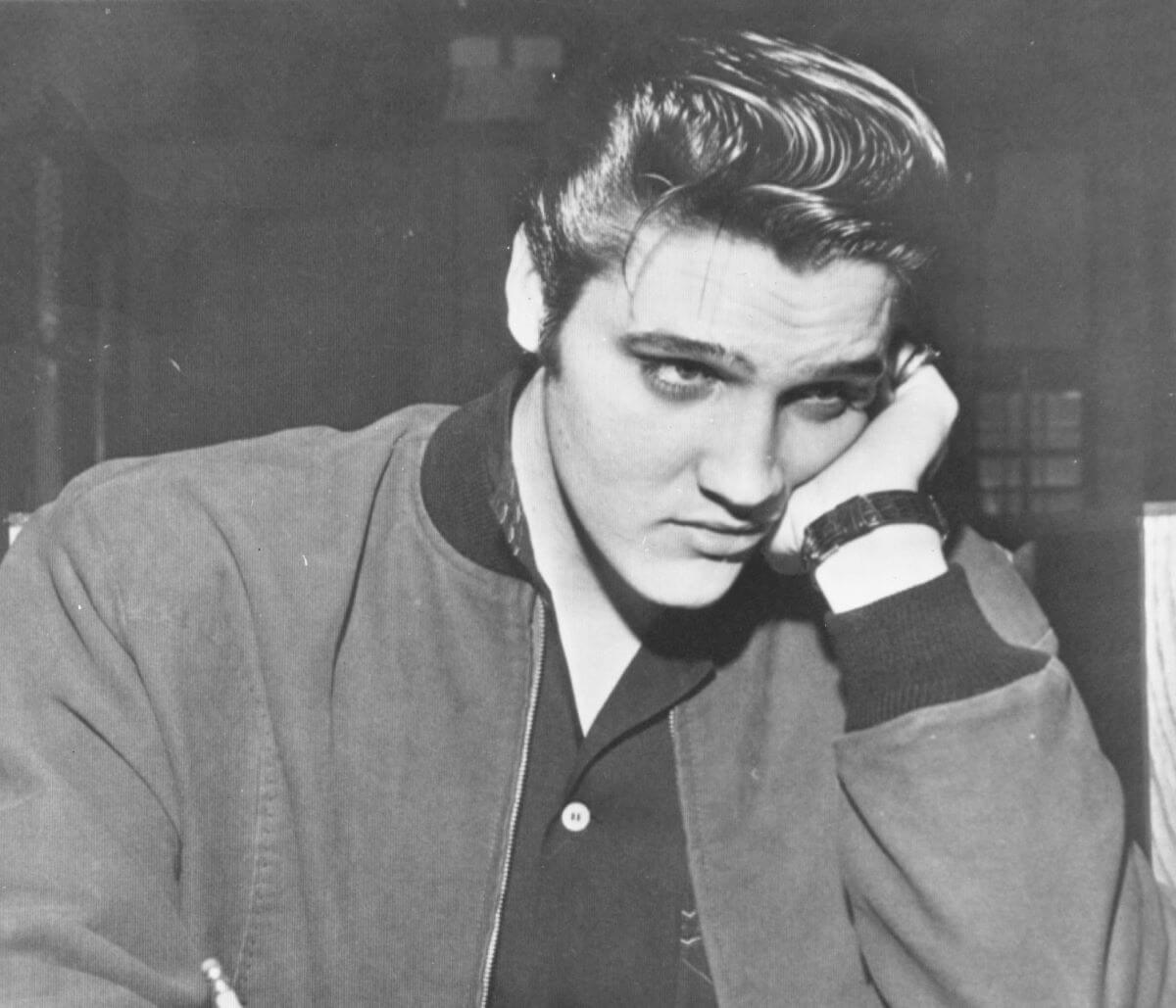 A black and white picture of Elvis Presley resting his face in his hand.