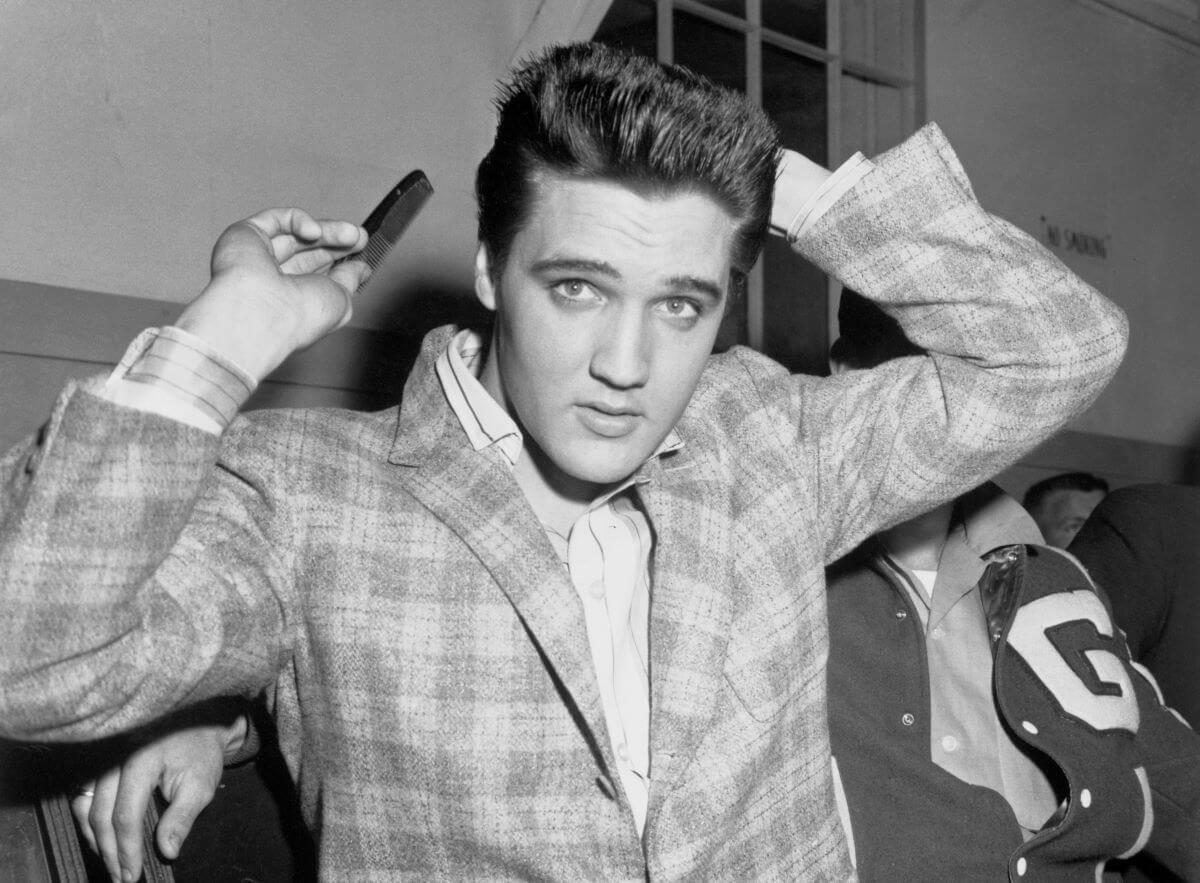 A black and white picture of Elvis Presley wearing a plaid suit and combing his hair.