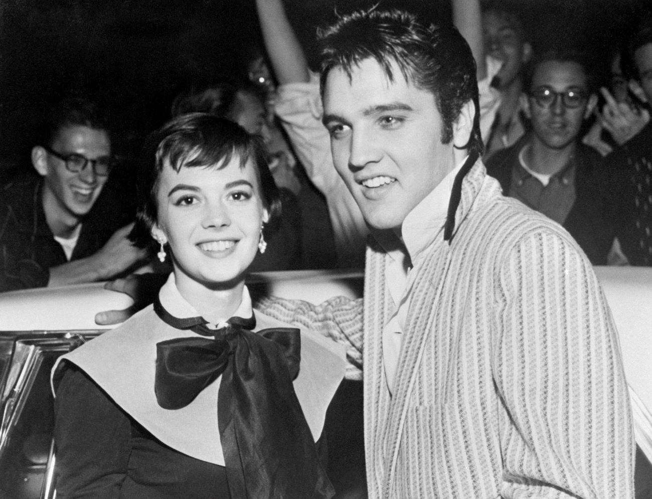 A black and white picture of Natalie Wood and Elvis Presley smiling at the camera while standing in front of a crowd.