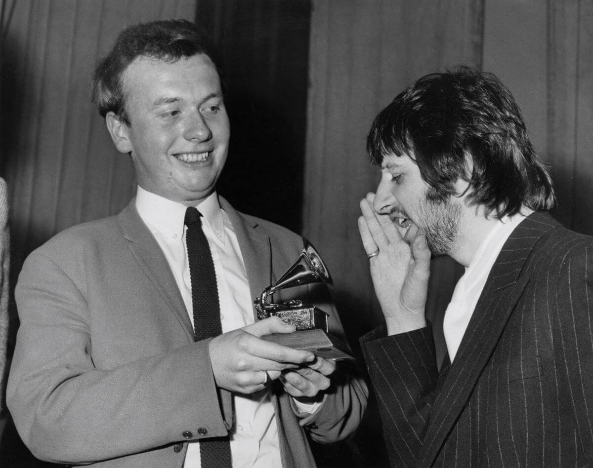 A black and white picture of Geoff Emerick holding a Grammy while Ringo Starr pretends to shout into it.