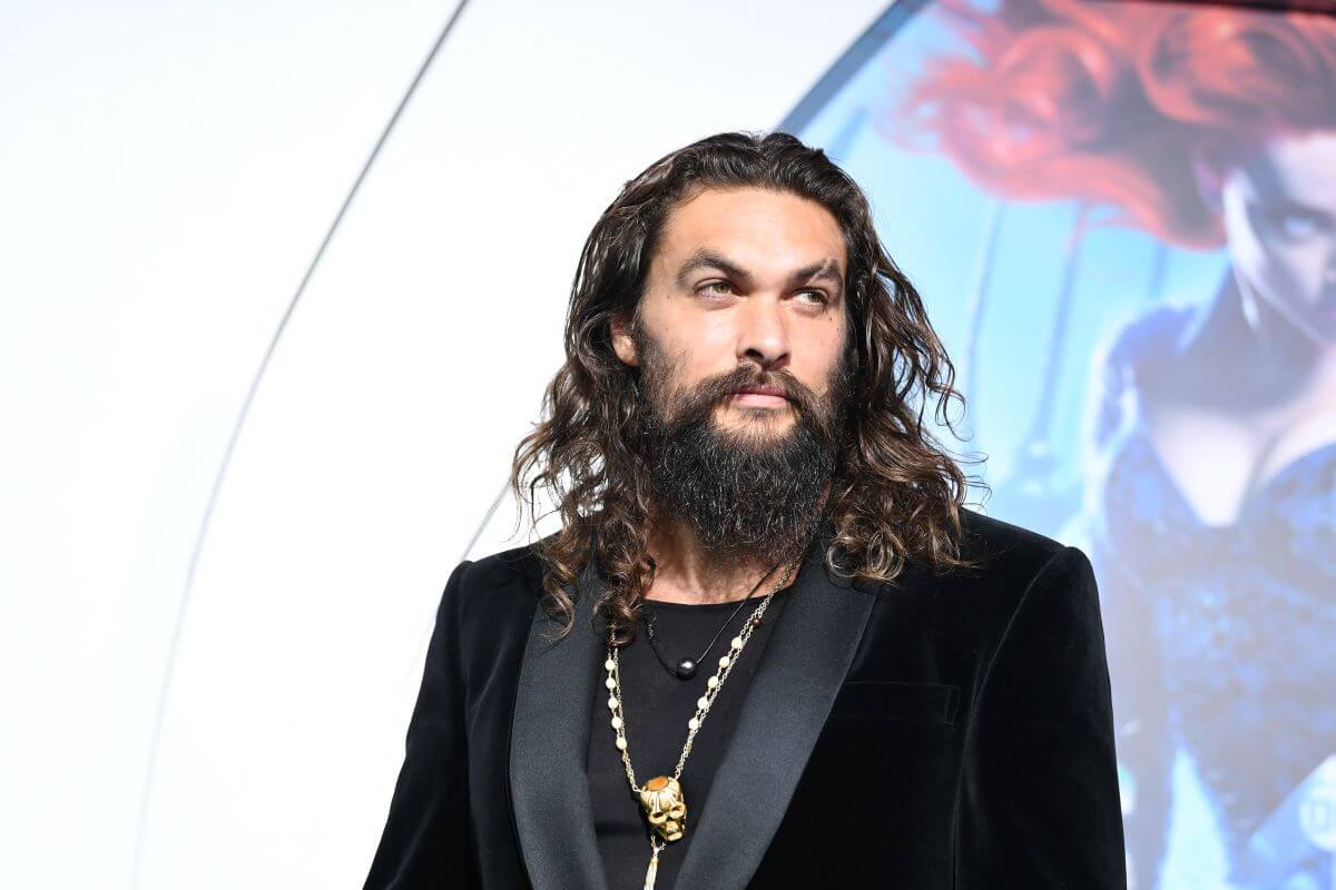 Jason Momoa wears a black suit and necklace.