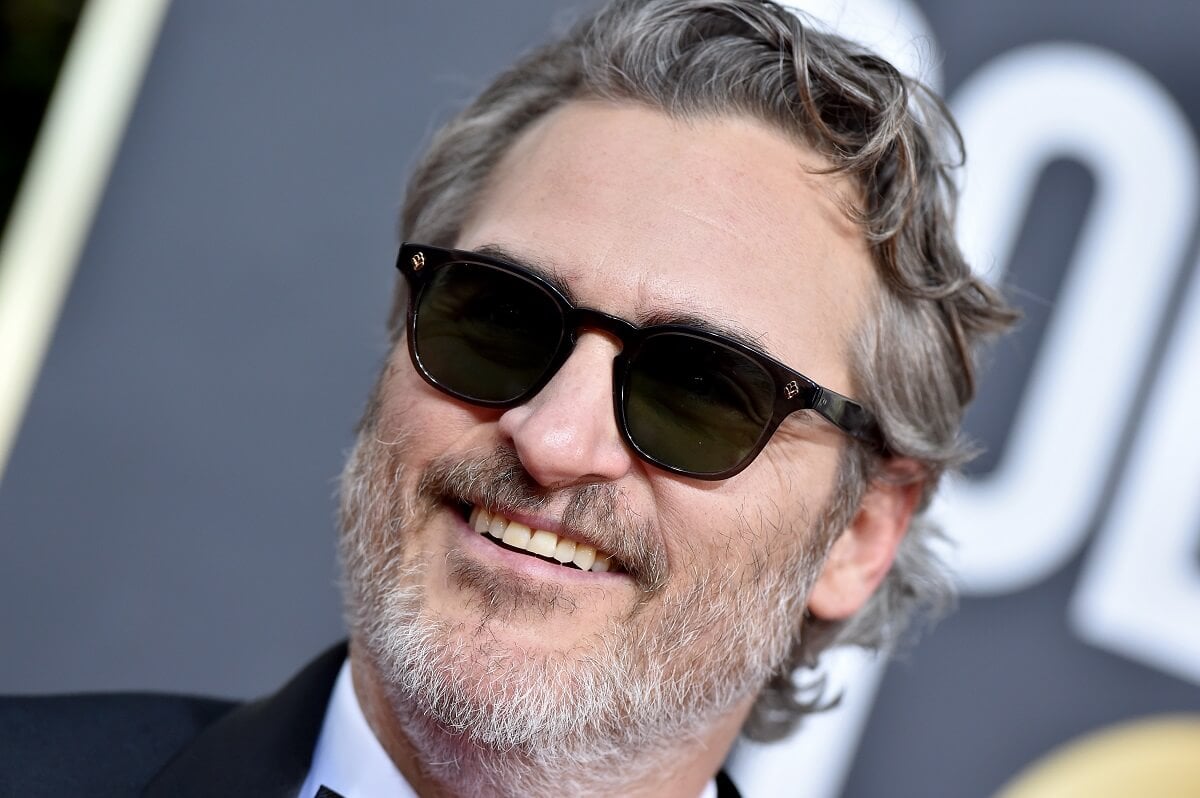Joaquin Phoenix smiling at the Golden Globes while wearing sunglasses.