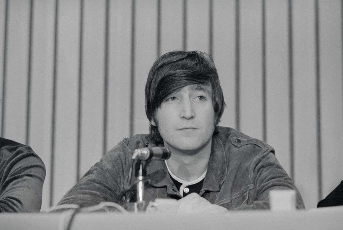 John Lennon sits in front of a microphone.
