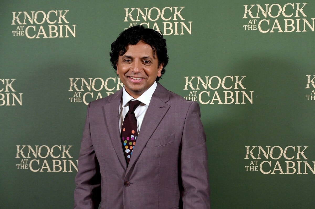 M. Night Shyamalan wearing a suit while taking a picture at the premiere of 'Knock at the Cabin'.