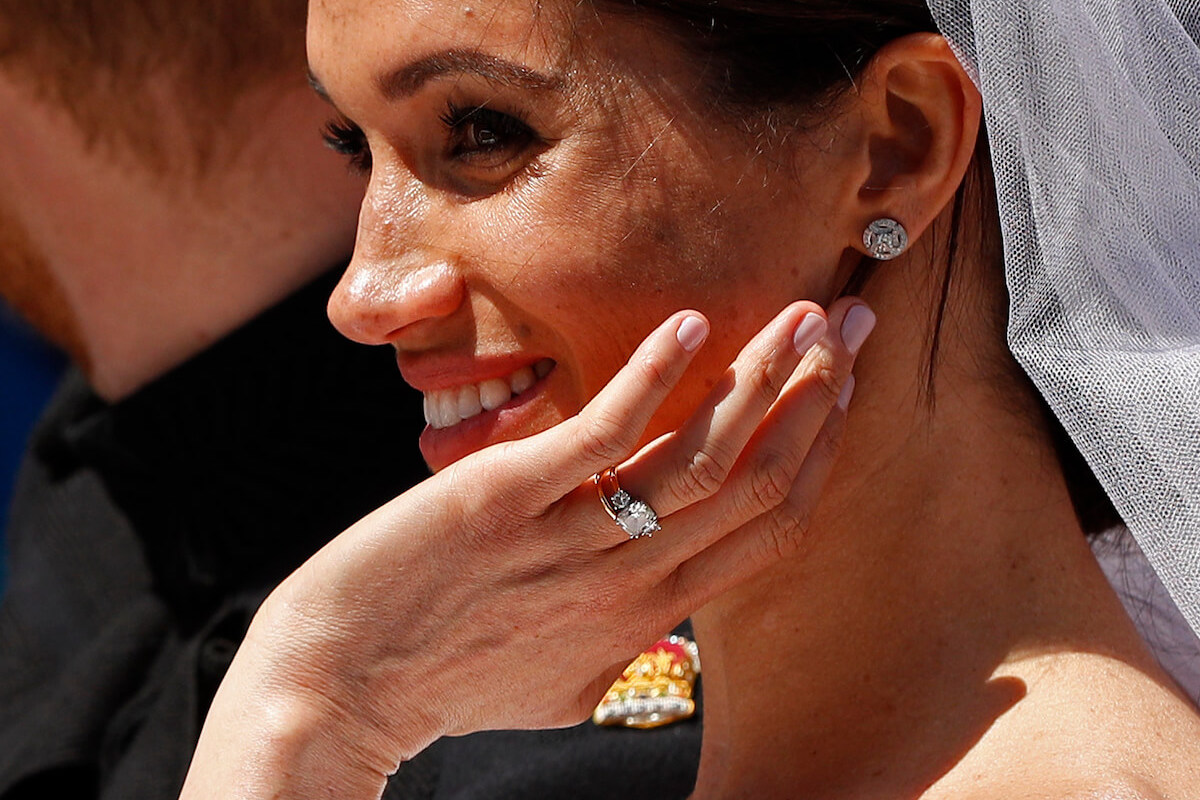 Meghan Markle, whom a commentator says may not be wearing her engagement ring from Prince Harry for practical reasons, smiles holding up her hand at her 2018 royal wedding