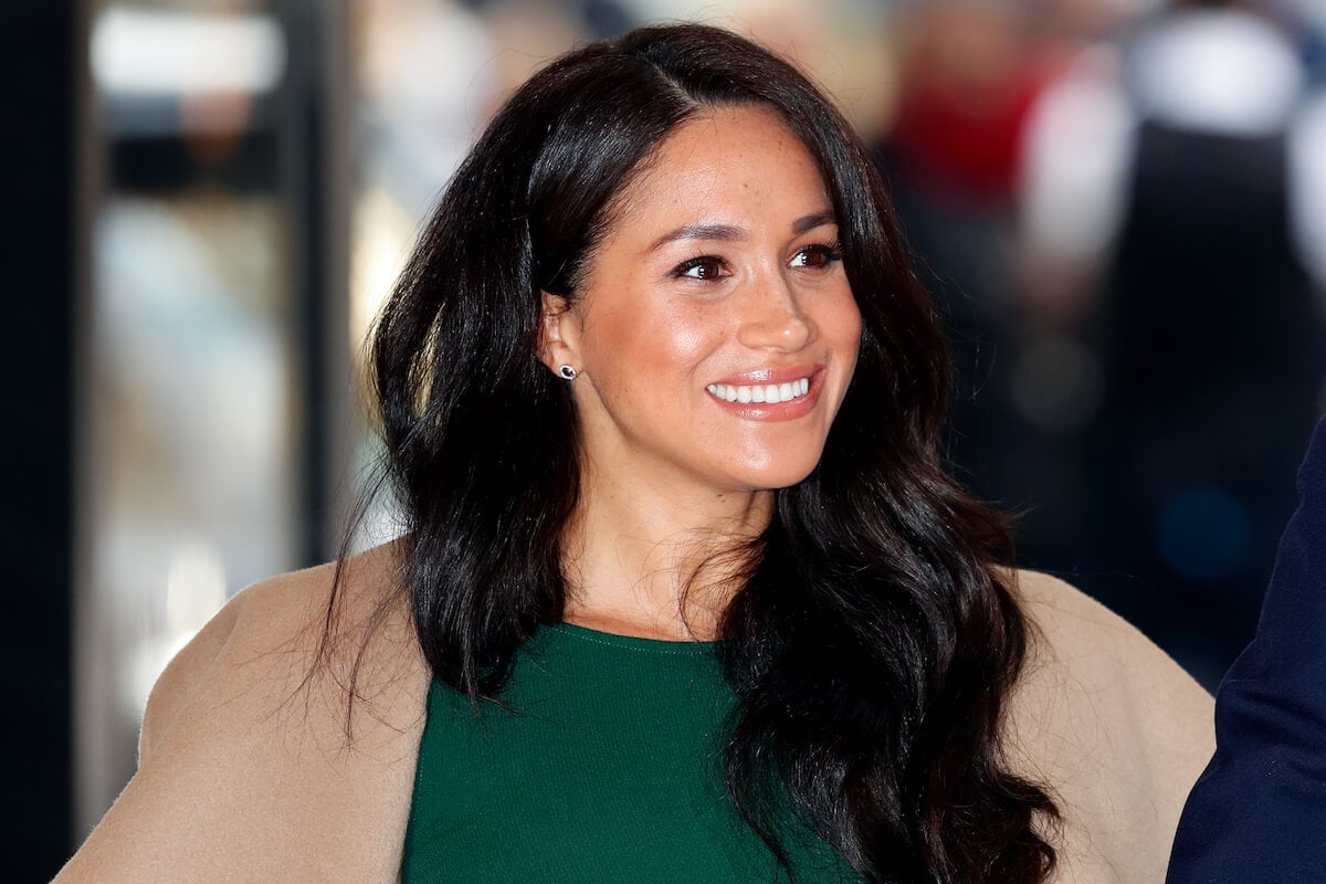 Meghan Markle, whose fondness for wearing coats in warm temperatures is 'odd,' according to a fashion expert, smiles and looks on