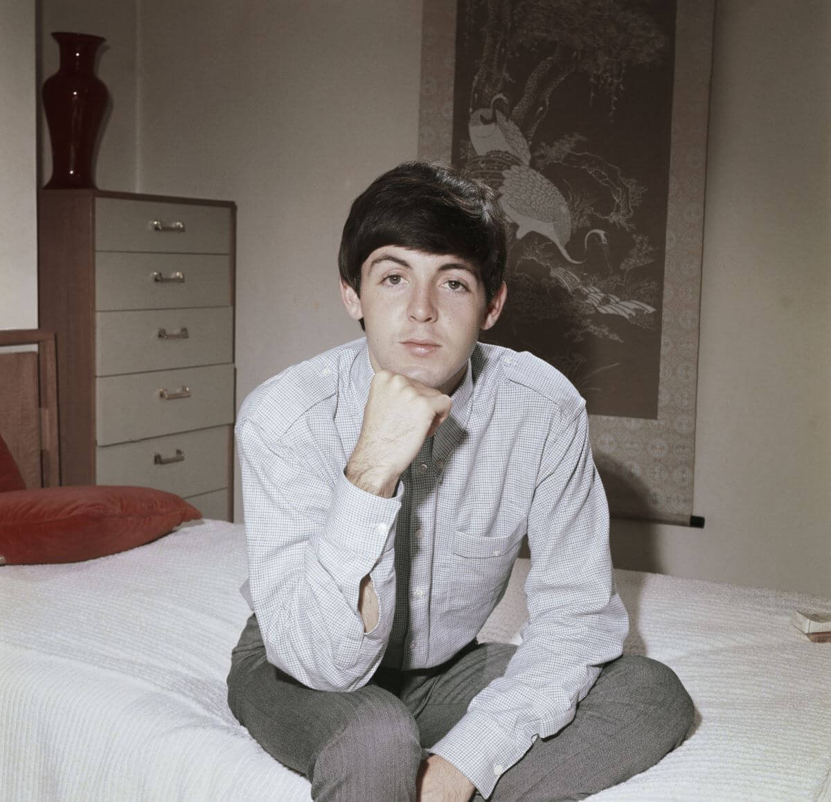 Paul McCartney sits on a bed. He rests his chin on his fist and his elbow on his thigh.