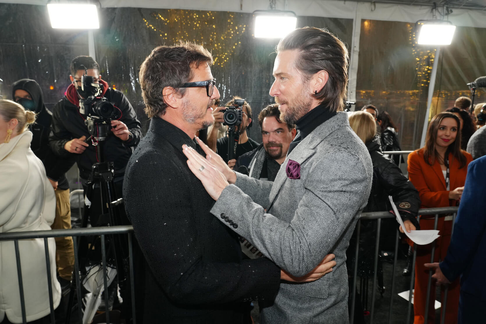 Pedro Pascal and voice actor Troy Baker from 'The Last of Us' embracing each other at a press event