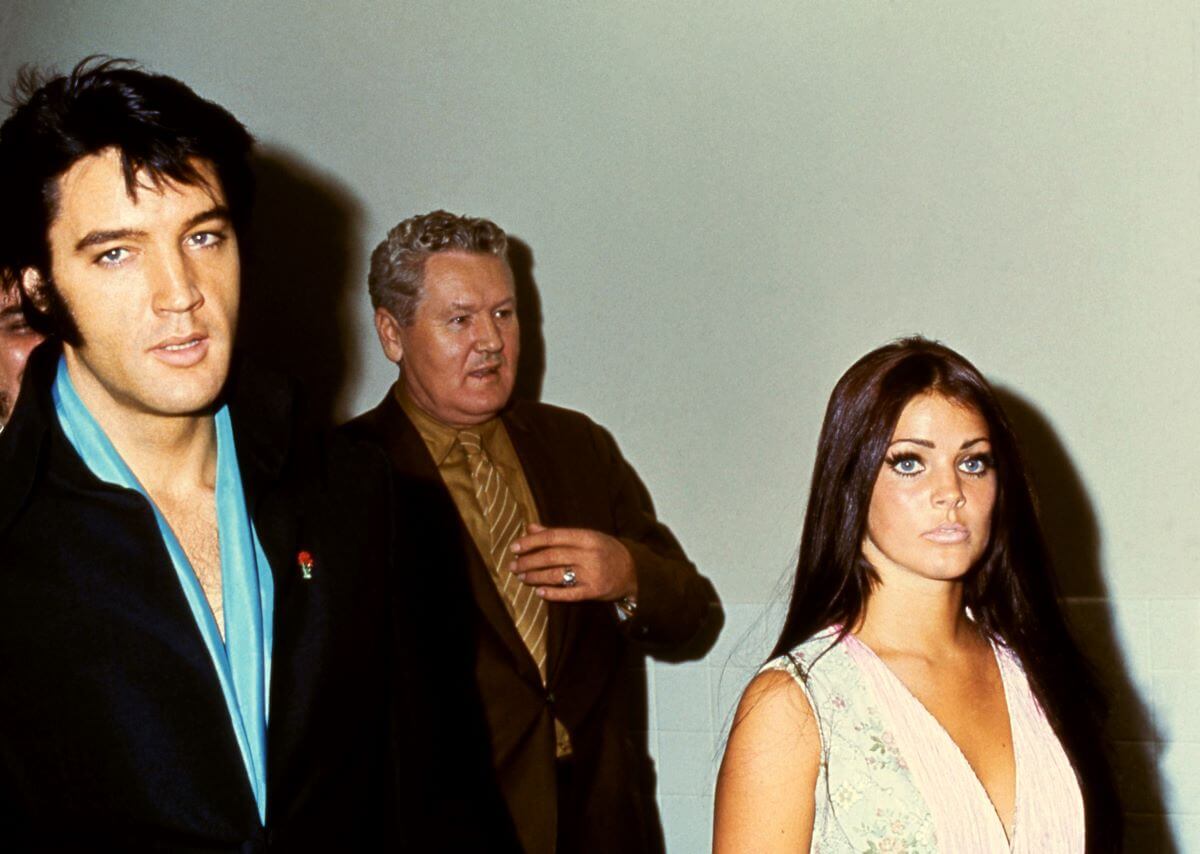 Elvis Presley, Elvis' father Vernon Presley, and Priscilla Presley walk down a hallway together.