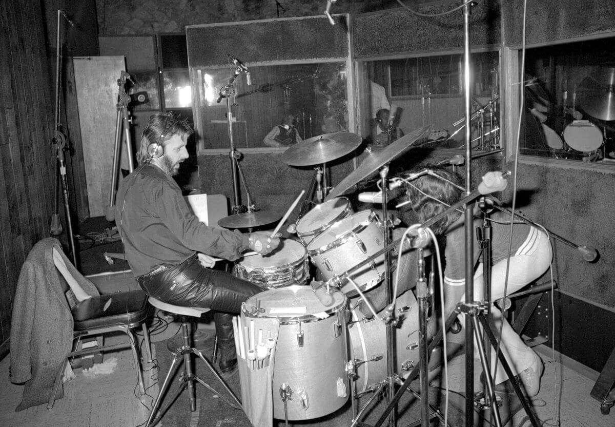 A black and white picture of Ringo Starr wearing headphones and drumming in the studio.