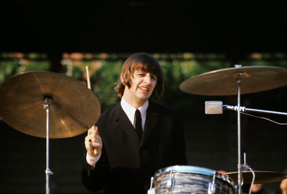 Ringo Starr wears a suit and drums at a concert.