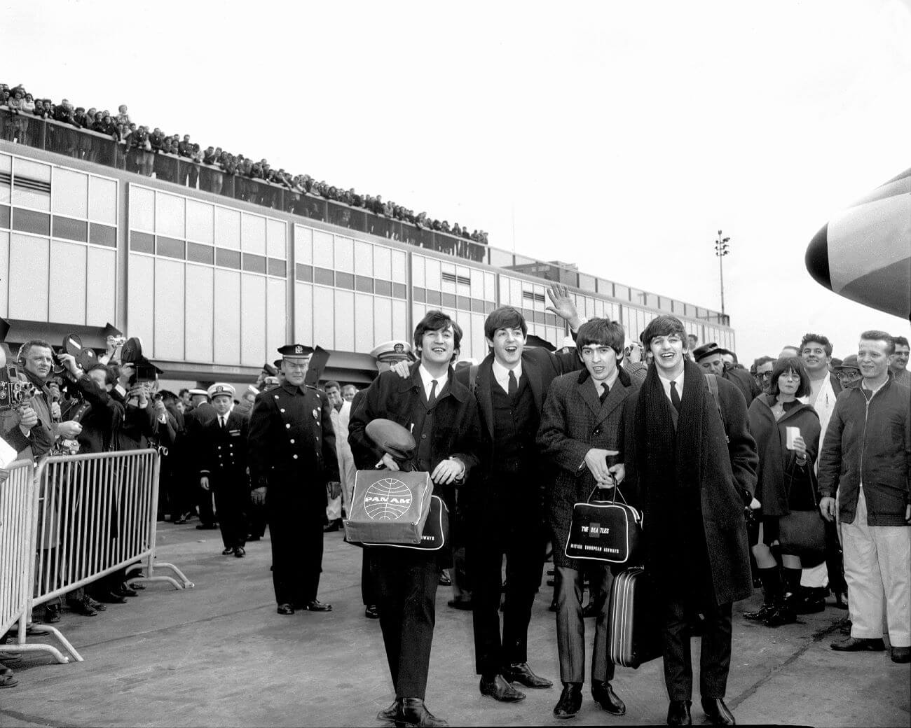 A black and white picture of The Beatles walking together at an airport while a large crowd watches them.