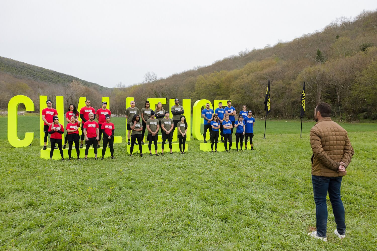 'The Challenge: USA' Season 2 cast members in red, blue, and green teams standing in front of TJ Lavin