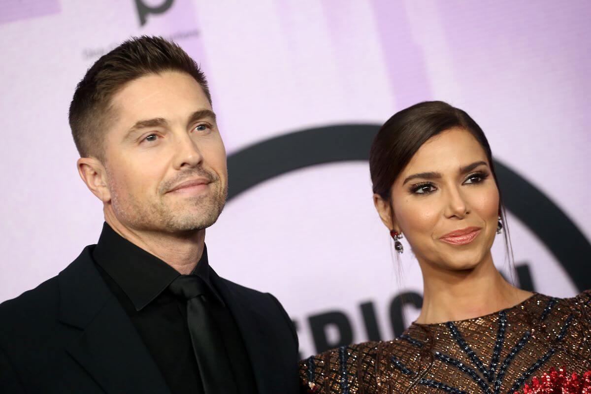 'The Rookie' star Eric Winter and Roselyn Sanchez wear black and pose in front of a purple background.