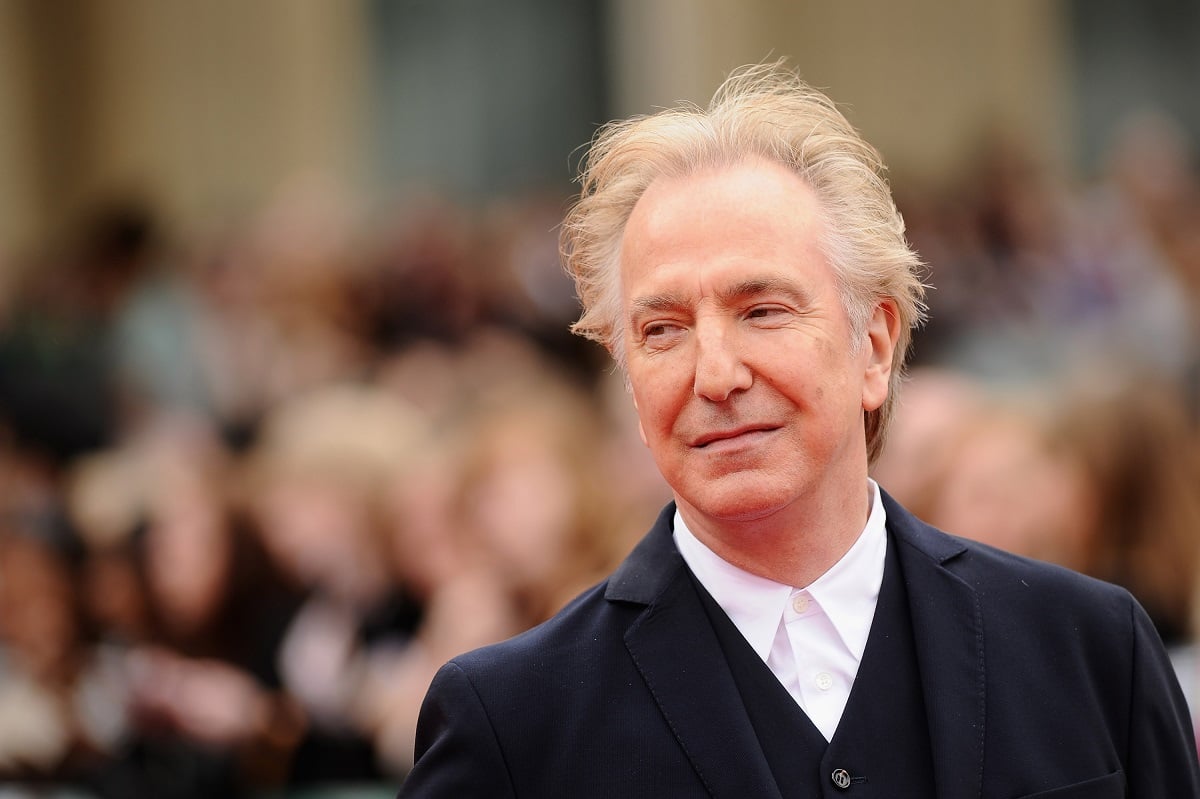 Alan Rickman posing in a suit at the World Premiere of 'Harry Potter and The Deathly Hallows' with a crowd behind him.