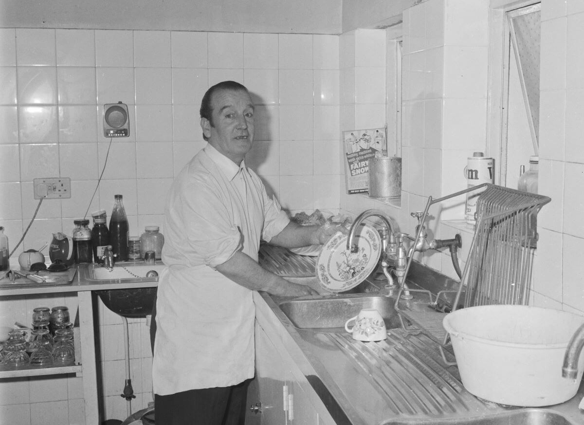 A black and white picture of John Lennon's dad, Alfred Lennon, washing dishes.