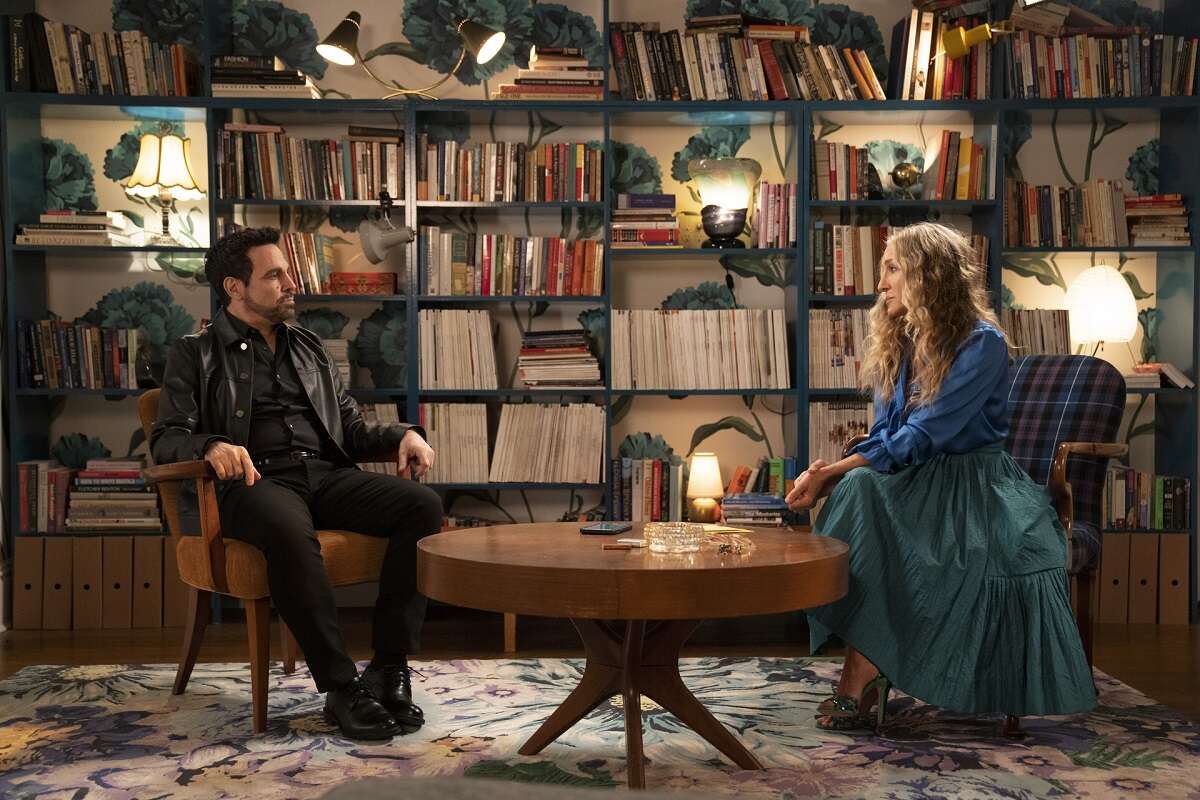 Anthony Marantino and Carrie Bradshaw sit together in her living area in front of a bookcase in season 1 of 'And Just Like That...'