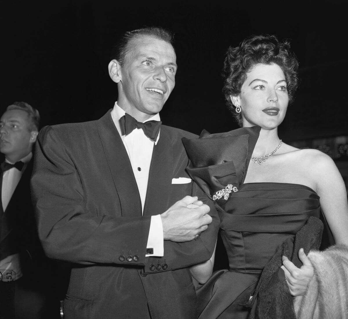 A black and white picture of Frank Sinatra wearing a tuxedo. Ava Gardner wears a dress and holds his arm.