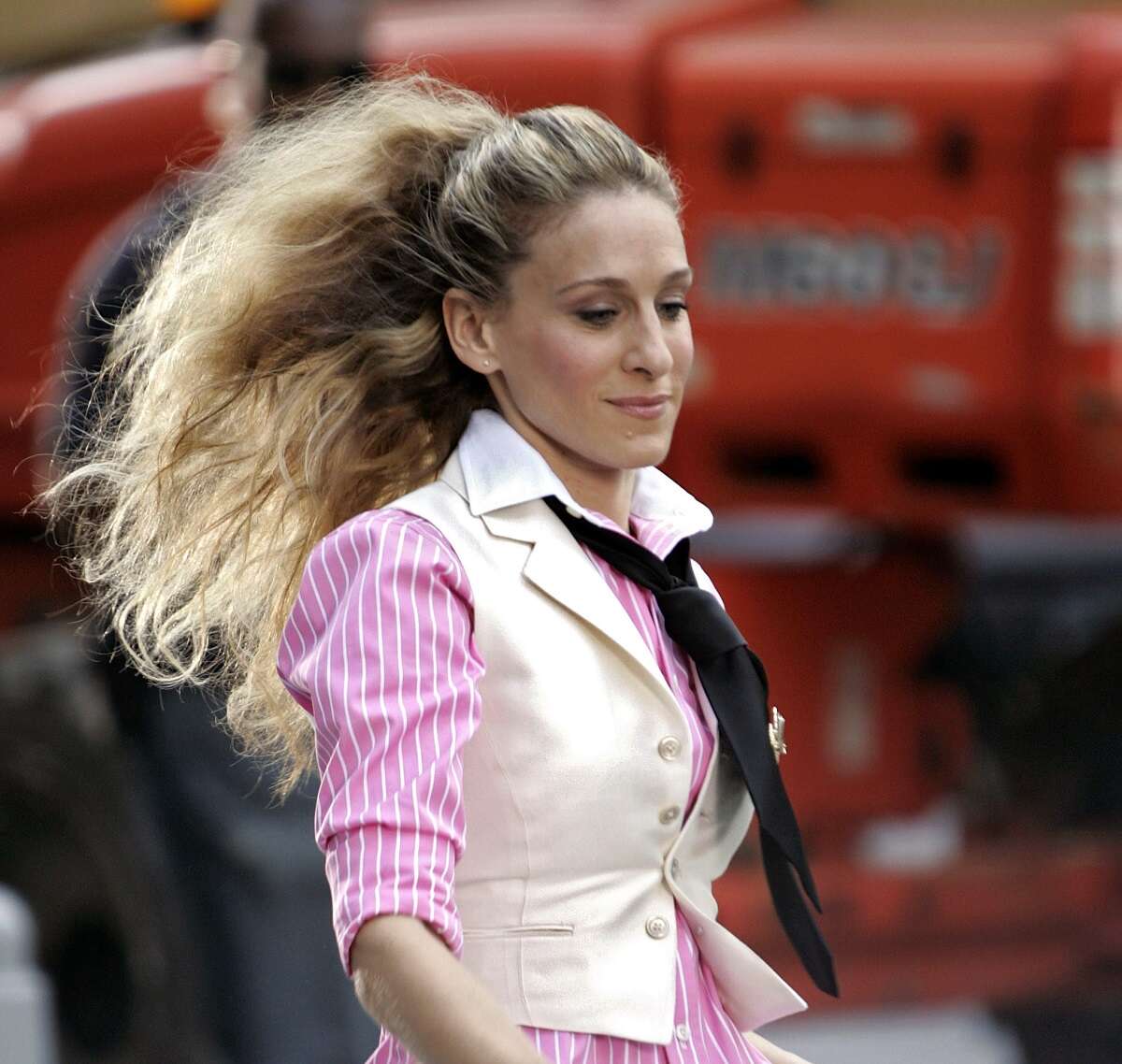 Carrie Bradshaw walks through Manhattan while filming of 'Sex and the City: The Movie,' wearing a white blazer and pink striped button-up