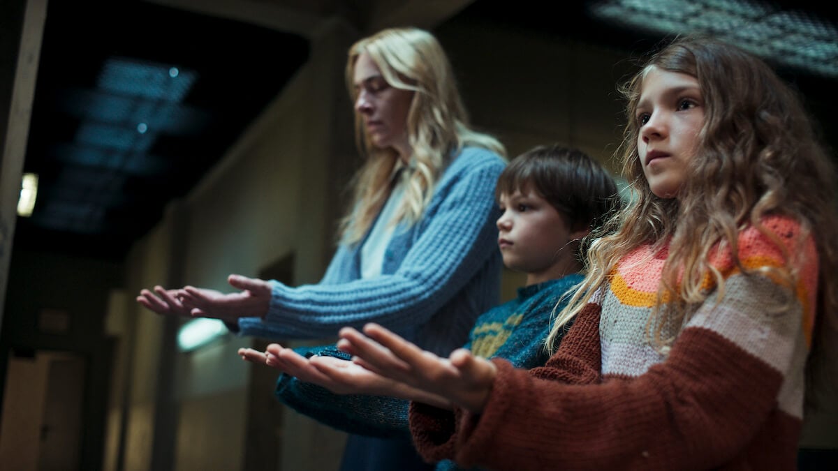 A blond woman and two children holding out their hands in 'Dear Child' on Netflix.
